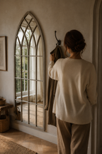 Femme de dos ajustant un manteau devant l'arche de ferme gris rustique, lumière du matin