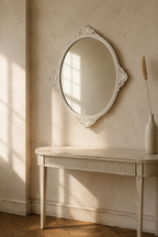 Ovale baroque blanc vieilli, ferronnerie délicate, au-dessus d'une console au mur en plâtre