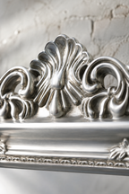 Détail macro du fronton en coquille sculptée et de la finition argentée de la psyché baroque