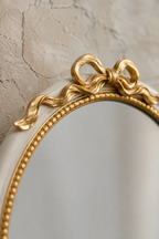 Détail macro du nœud doré sculpté et du liseré perlé de l'ovale blanc et or