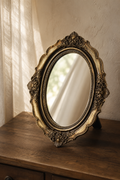 Miroir coiffeuse, baroque doré 17×21,5 cm, debout sur un bureau en bois grâce à son pied-support.